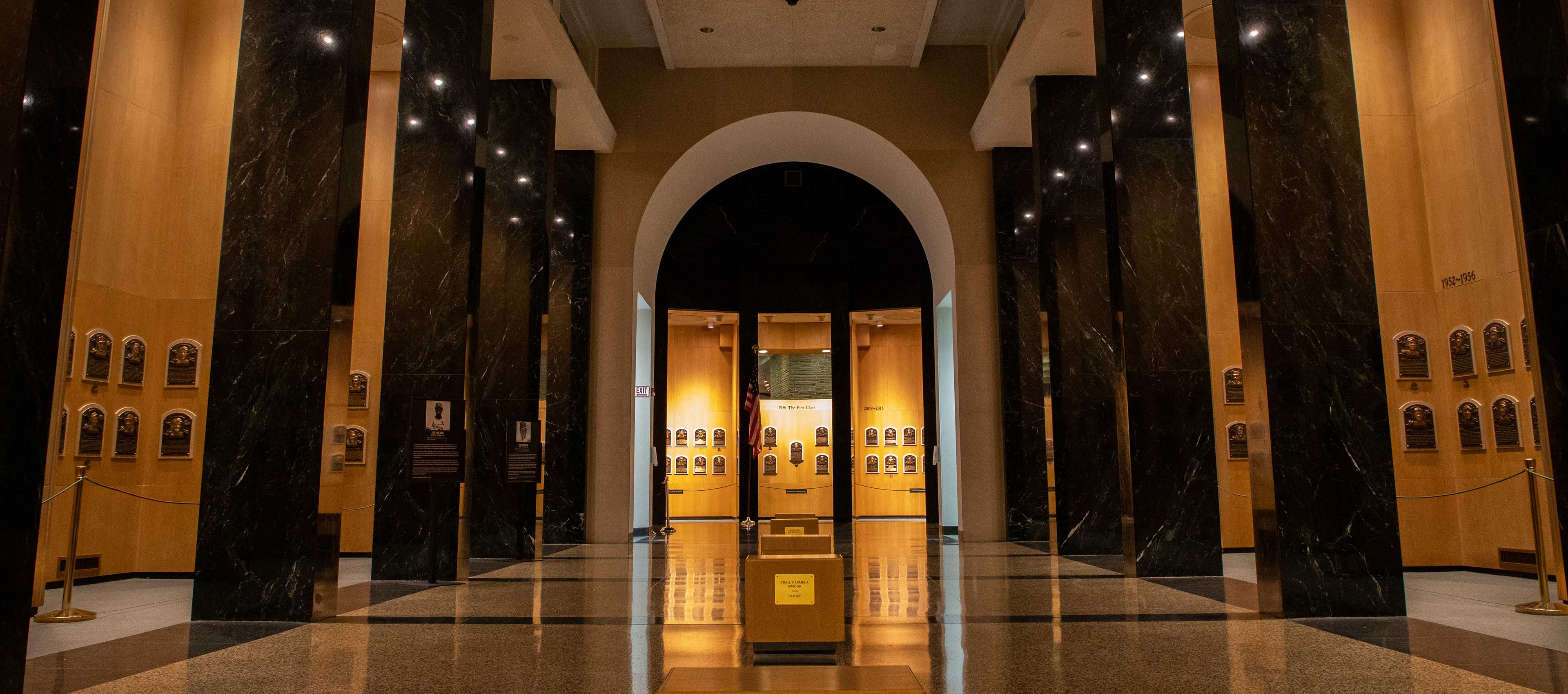 Interior of a hall of fame with bronze plaques on wooden walls and black marble columns.