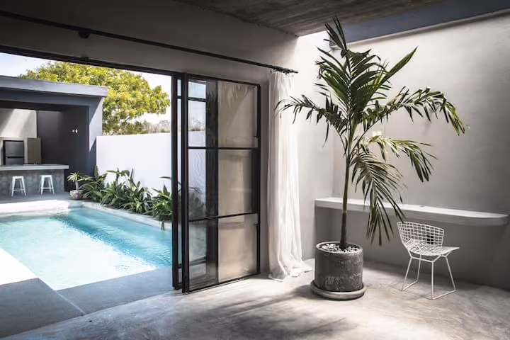 Palm tree in a pot by open glass doors leading to the pool at El Bungalow en Casa Nube Rosa