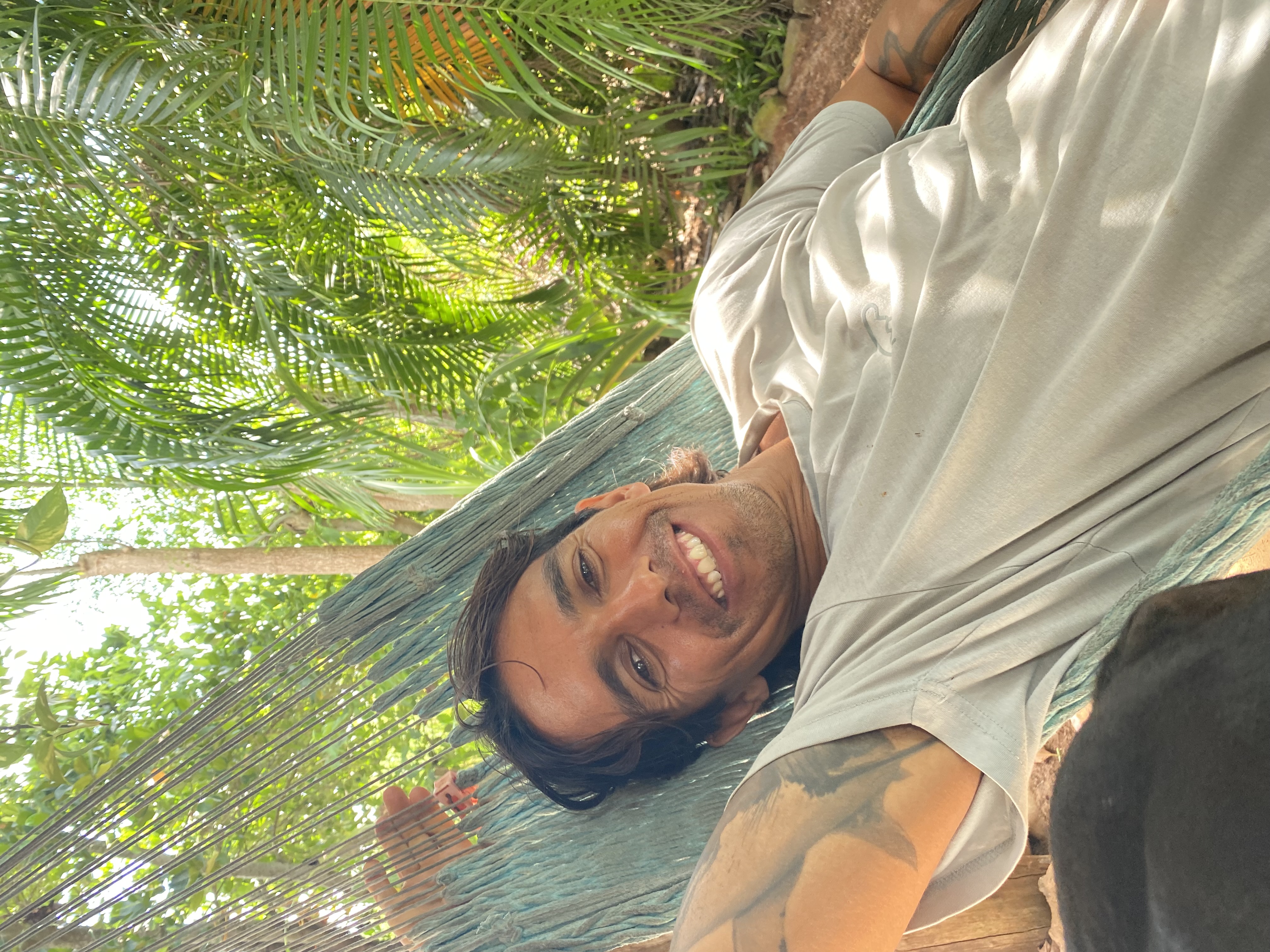 Cristo León smiling in a hammock under palm trees