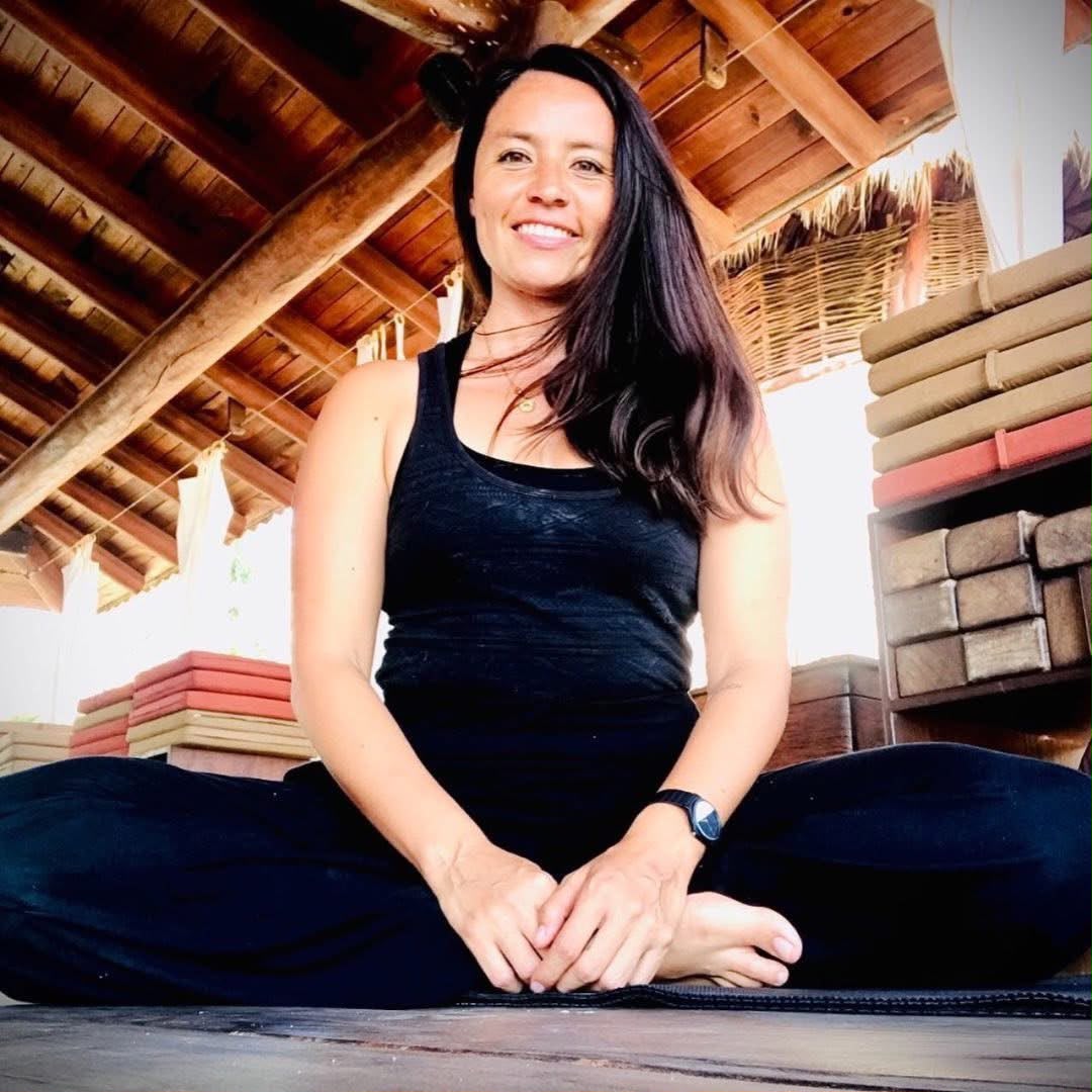 Fer seated cross-legged on a yoga mat under a palapa roof