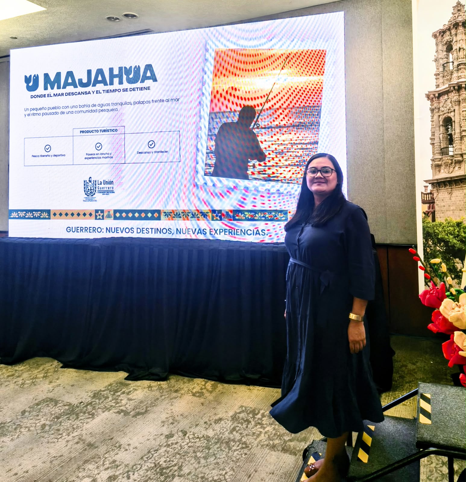 Yamel Maya standing beside a screen presenting Majahua as a tourism destination