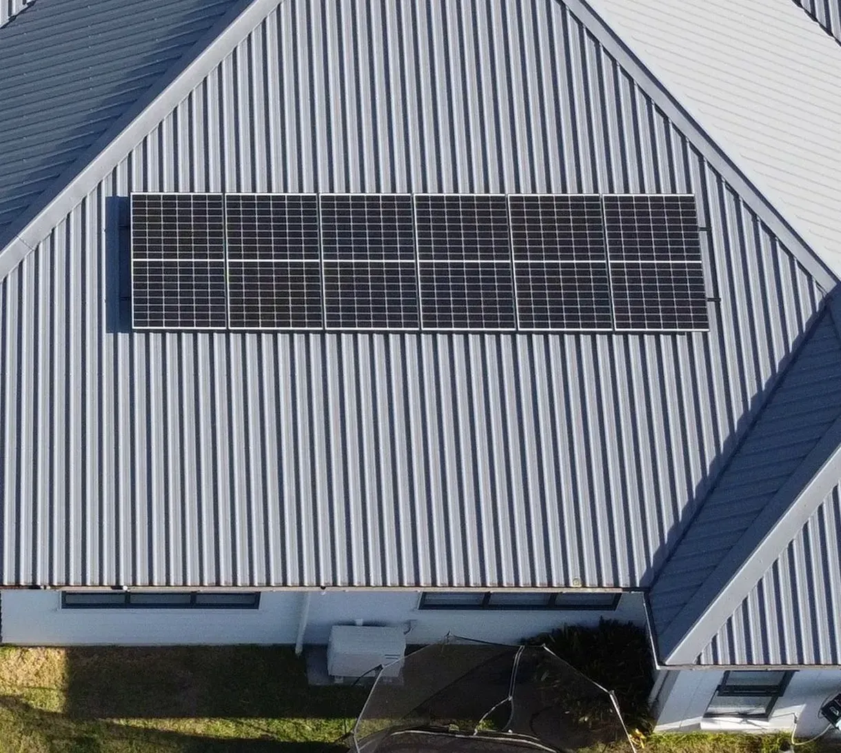 Aerial view of a corrugated metal roof with a row of solar panels installed horizontally near the top.