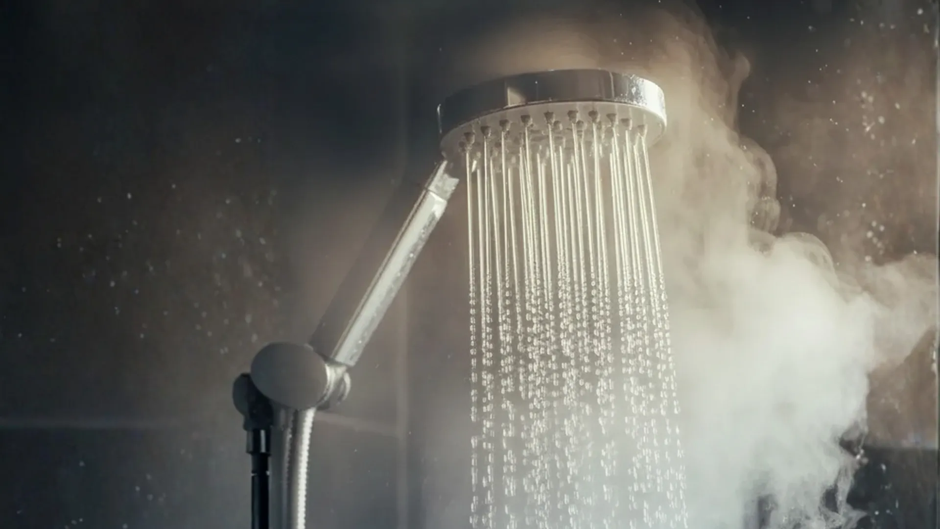 Silver shower head with water flowing and steam rising in the background.