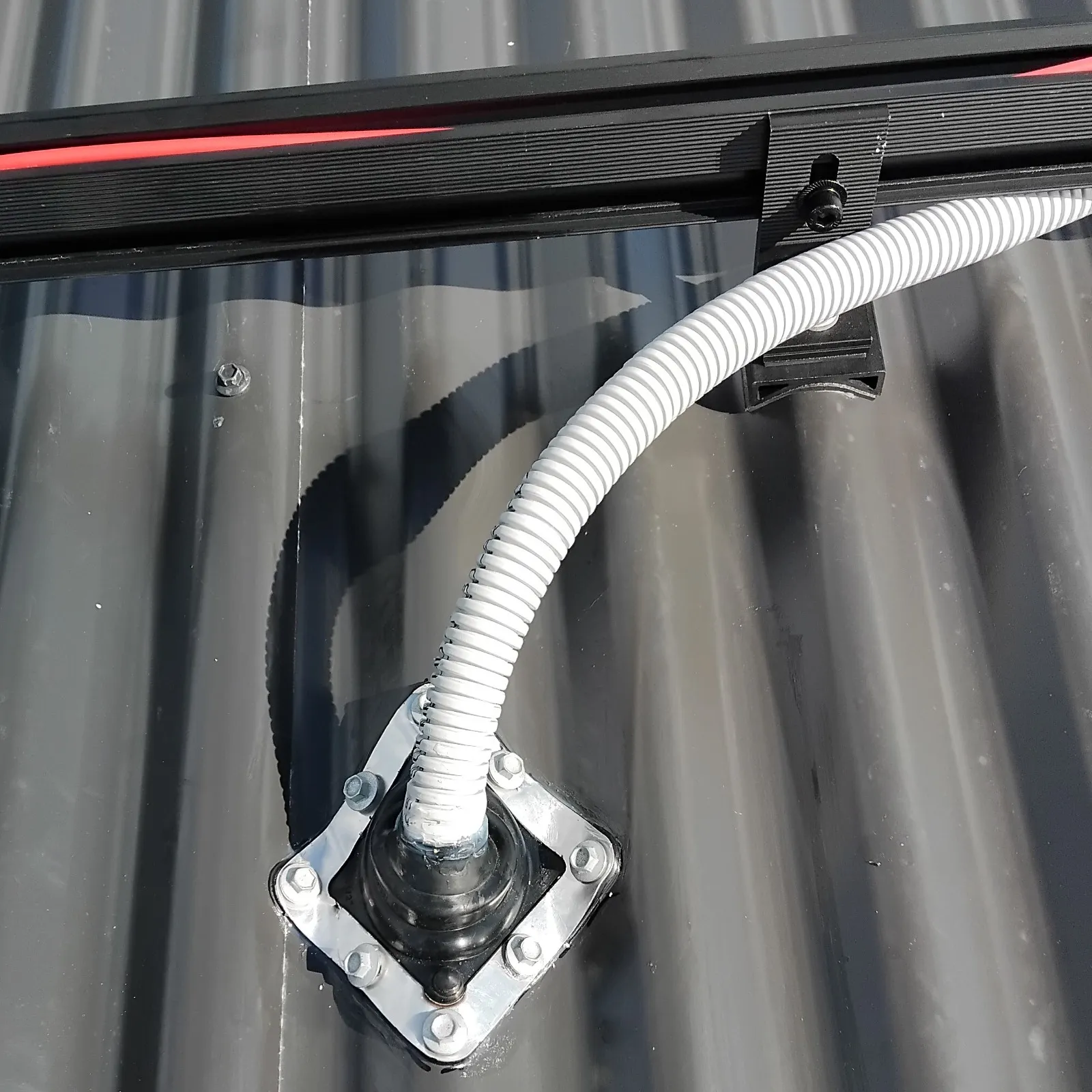 Flexible white conduit connected to a black roof flashing on a corrugated metal roof.