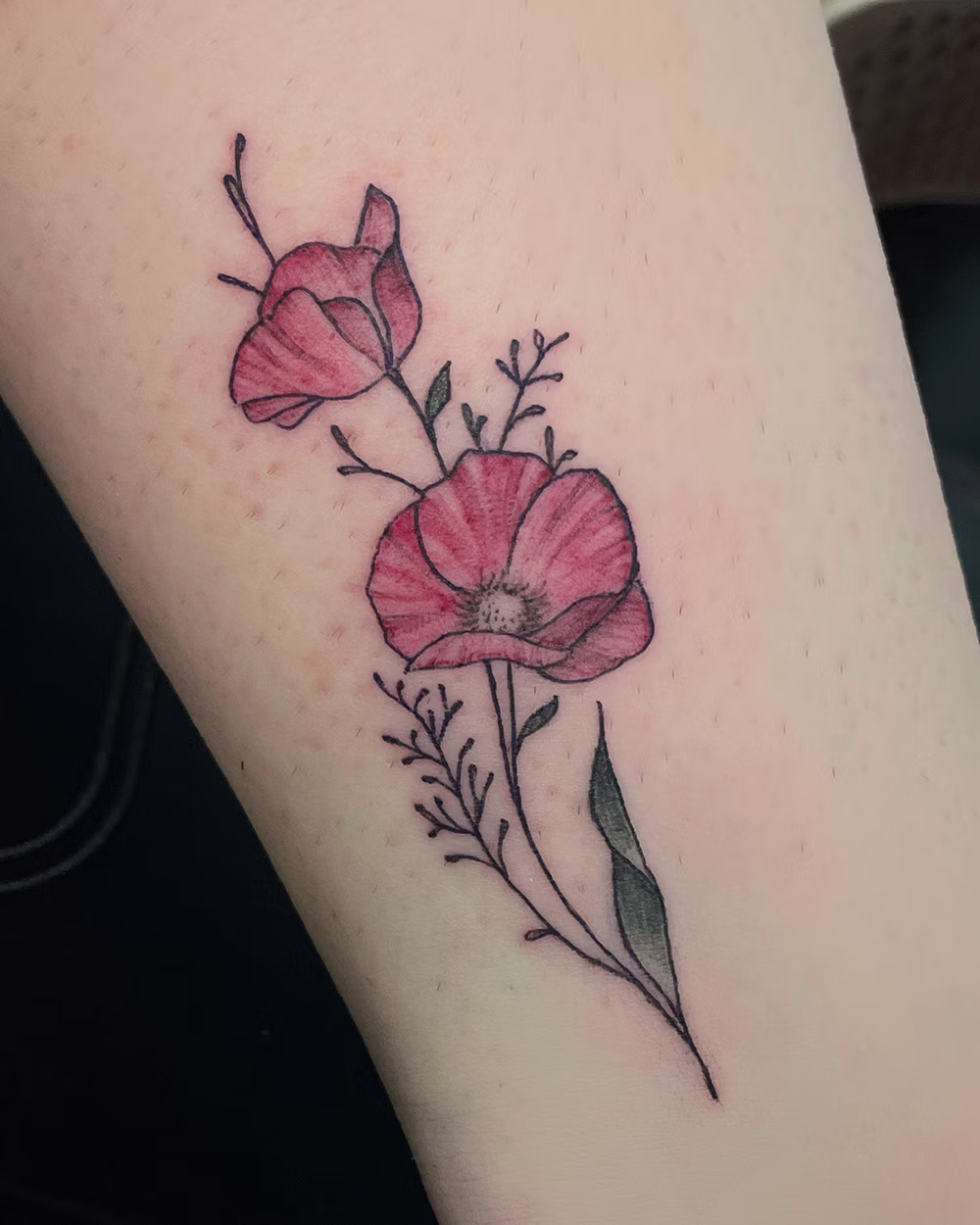 Tattoo of two pink flowers with thin stems and small leaves on light skin.