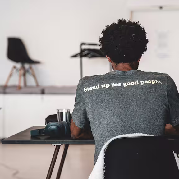 A young founder in a t-shirt is seen from behind as he works at a minimal modern desk.
