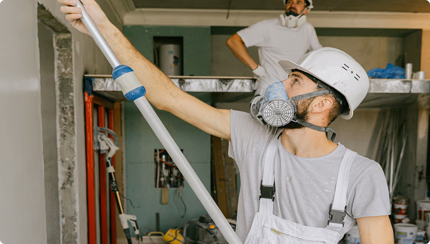 Man in white hard hat and respirator holds long pole