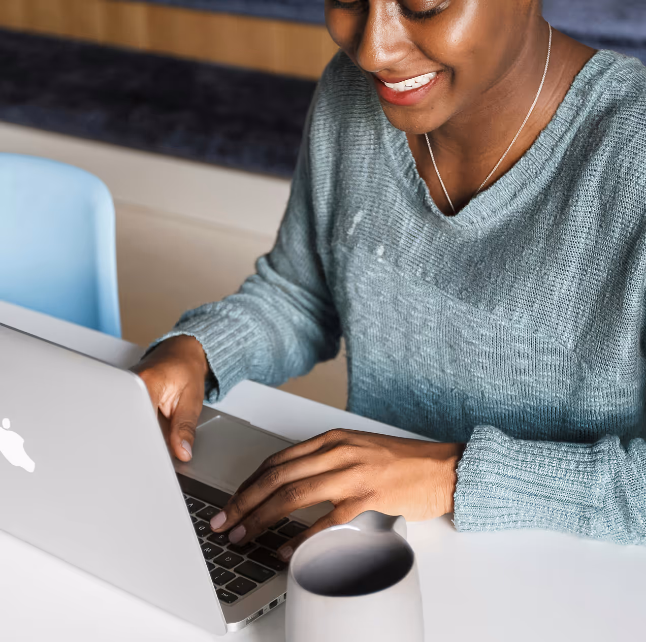 A smiling woman types on a silver laptop computer