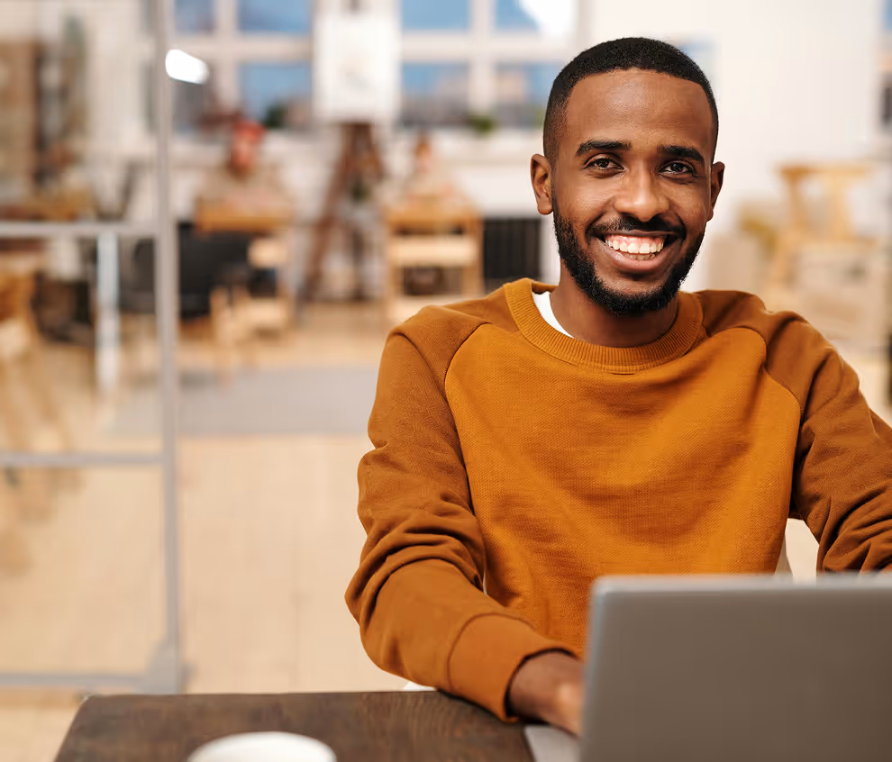 Smiling man with a beard wearing an orange sweater at desk