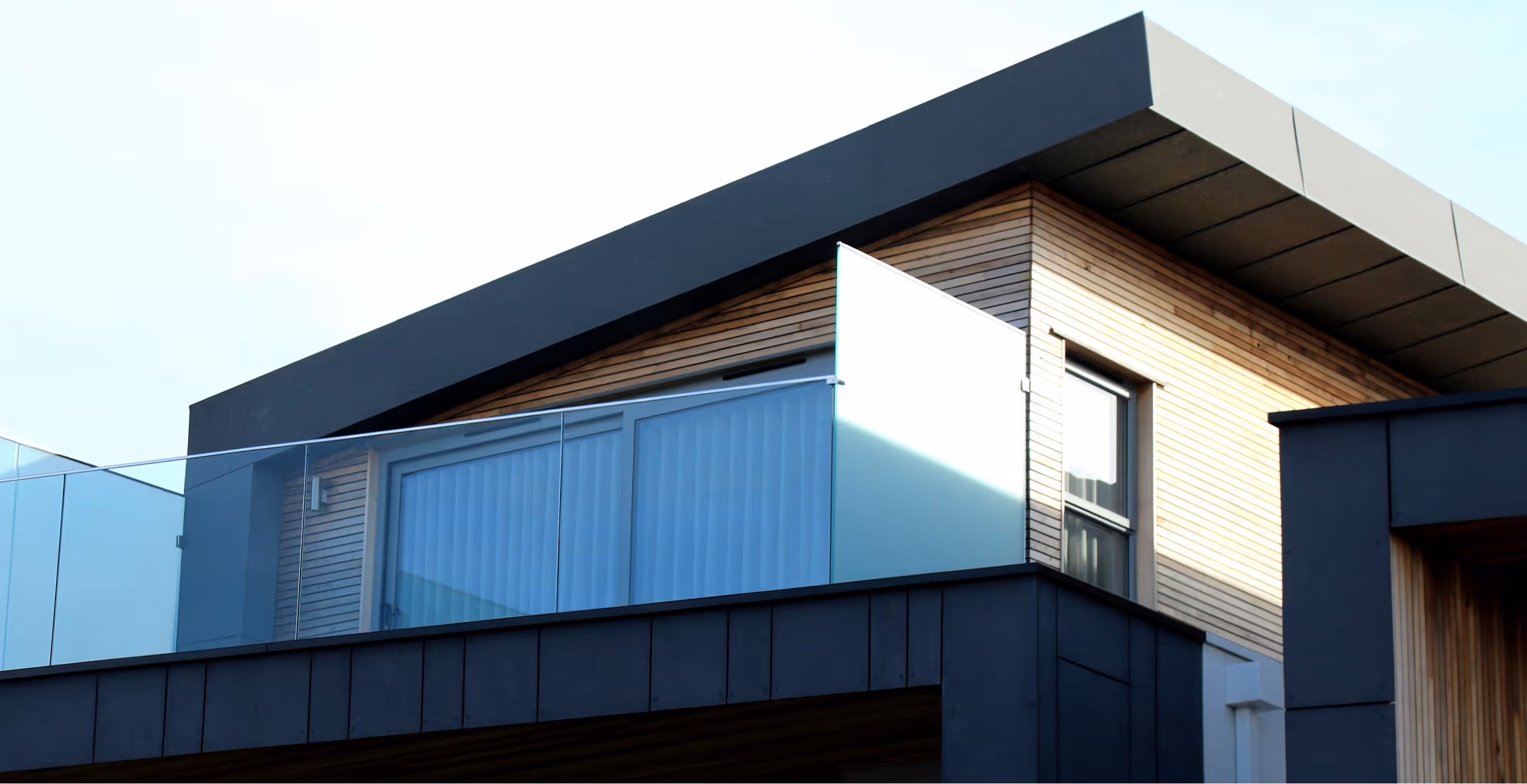 Modern house exterior with wooden siding, large glass windows, and a glass balcony railing.