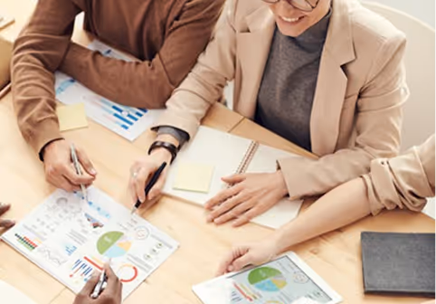 Three people collaborating at a table with charts, graphs, and notebooks during a meeting.