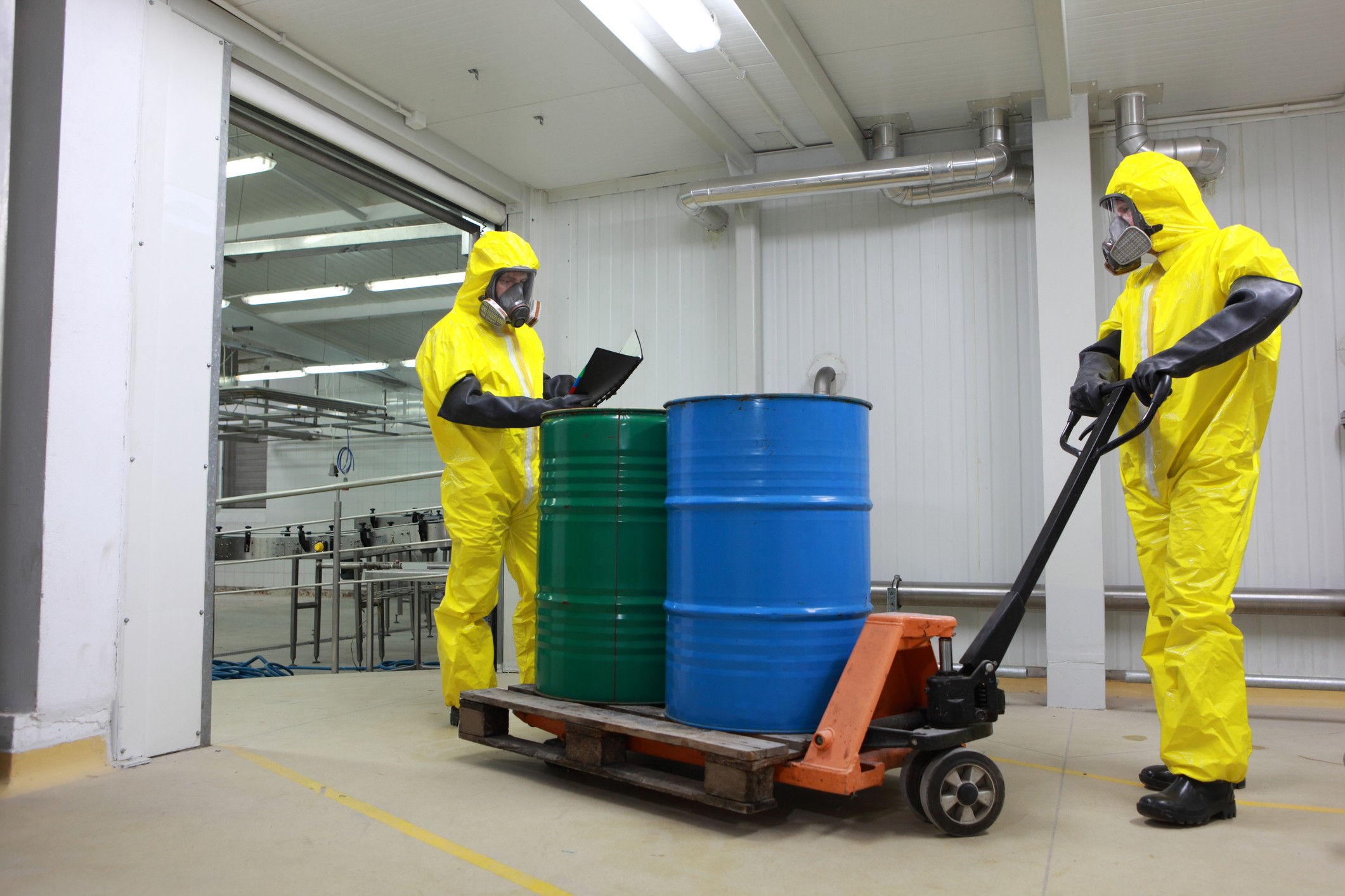 Workers in protective suits handling hazmat drums on a pallet jack for certified transport