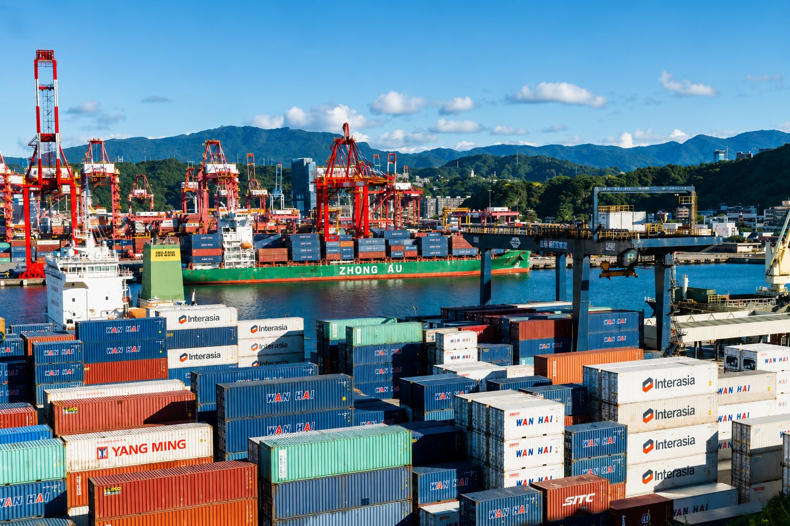 Stacked shipping containers in the foreground with a container ship, red cranes, and green mountains across the harbor in Taiwan
