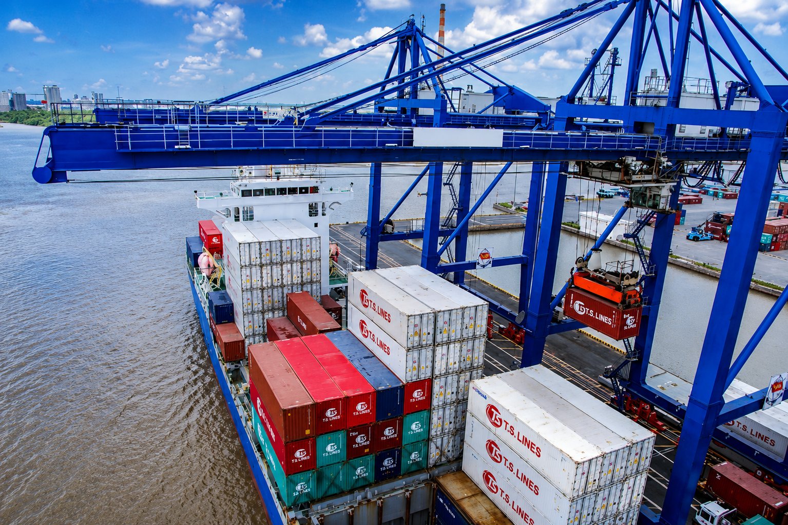 Blue quay crane lifting a shipping container from a loaded vessel at a river terminal in Vietnam