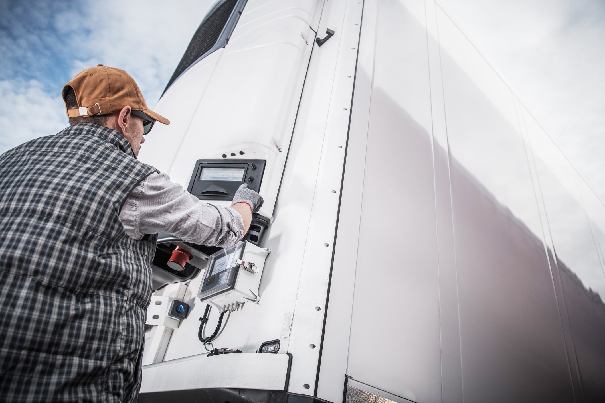 Driver checking the temperature control panel on the front of a white refrigerated trailer