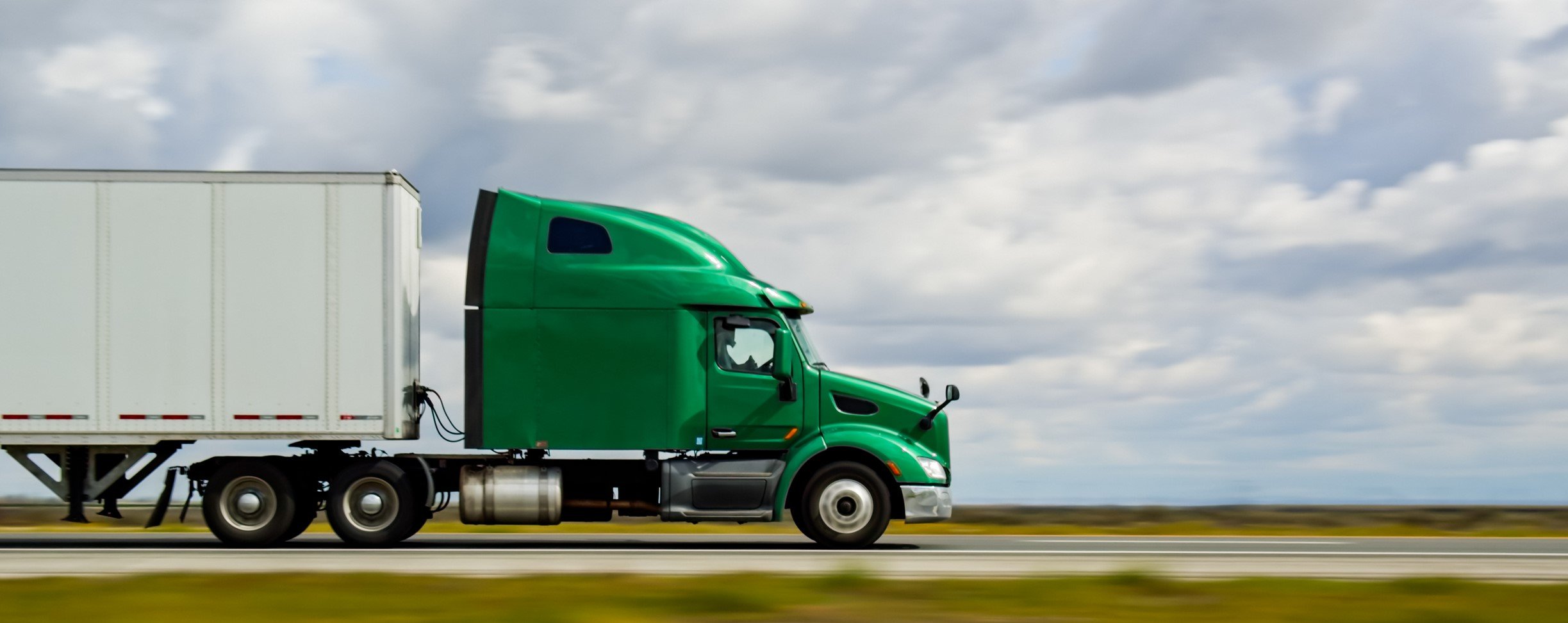 Green semi truck pulling a white dry van trailer on a highway, LTL freight shipped nationwide from Southern California by AEEM Shipping