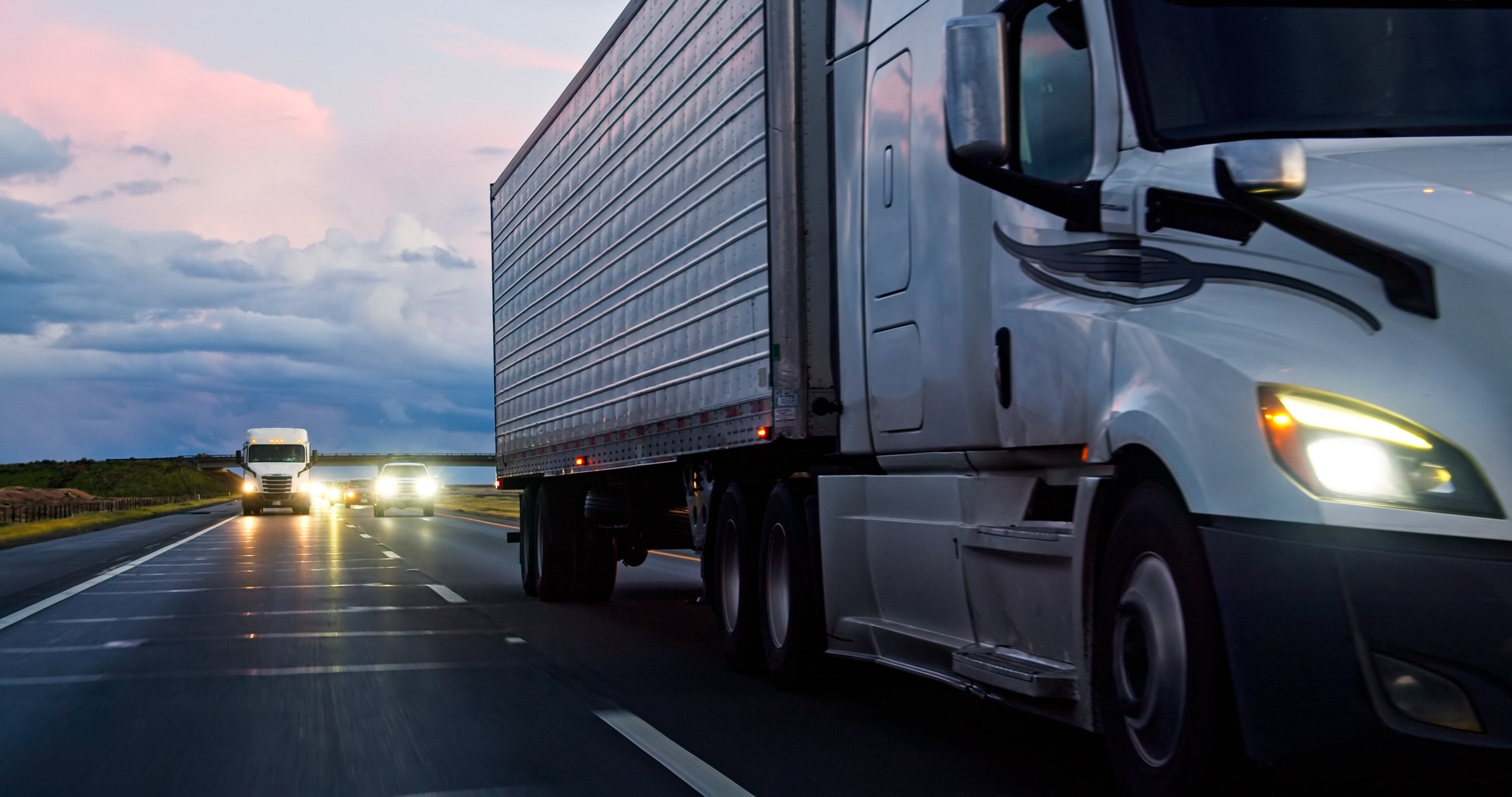White semi truck hauling a dry van trailer on a multilane highway at dusk, LTL freight moved nationwide from Southern California by AEEM Shipping