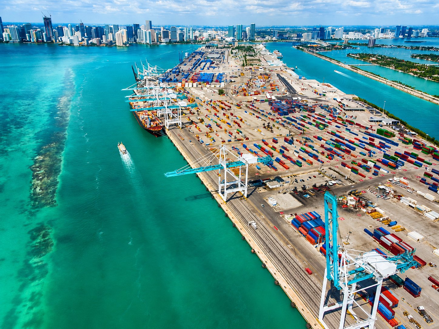 Aerial view of the PortMiami container terminal with gantry cranes, stacked containers, and the Miami skyline across the water, Florida