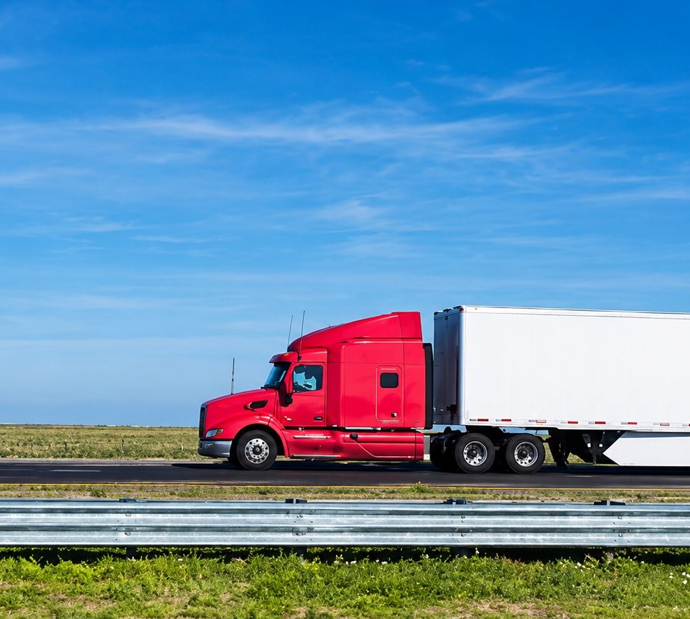 Red semi truck pulling a long white dry van trailer across flat green prairie under a wide blue sky, full truckload freight to Iowa