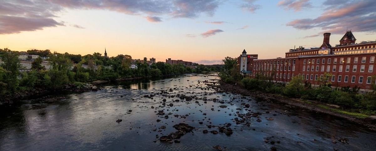 Historic brick mill buildings along the rocky Merrimack River at dusk in Manchester, New Hampshire