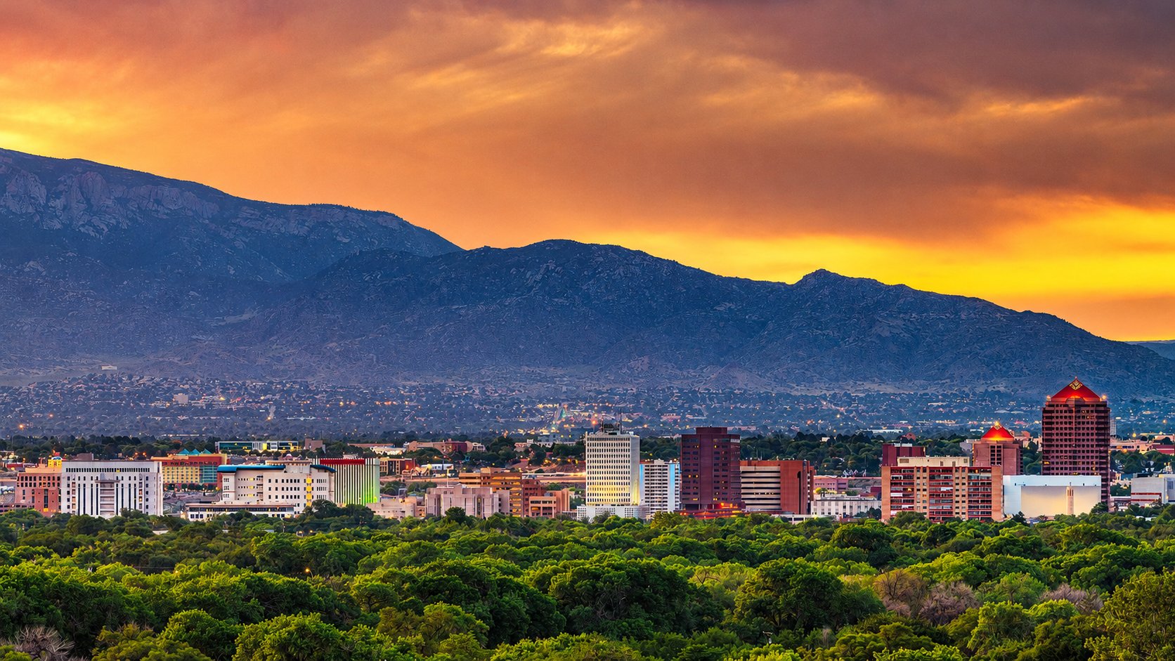 Albuquerque skyline at sunset with the Sandia Mountains rising behind the city and the cottonwood bosque in the foreground, New Mexico