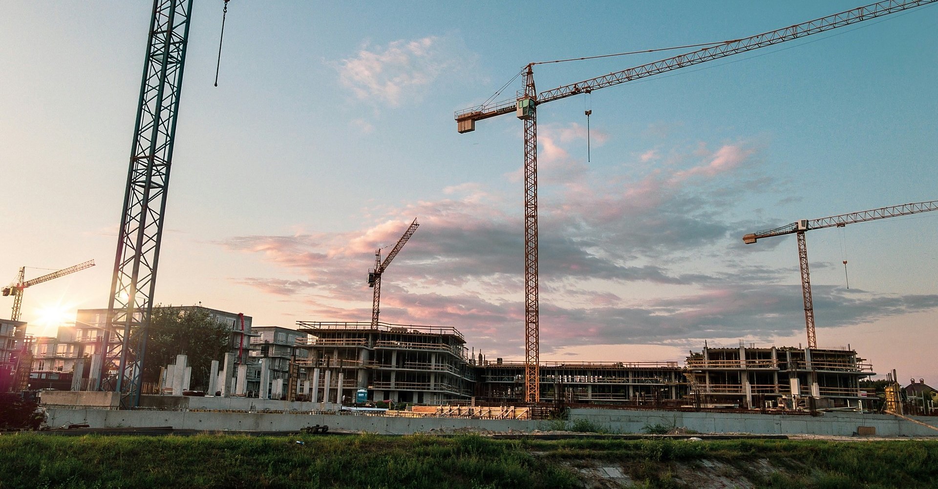 Tower cranes over a multi-building concrete construction site at sunset
