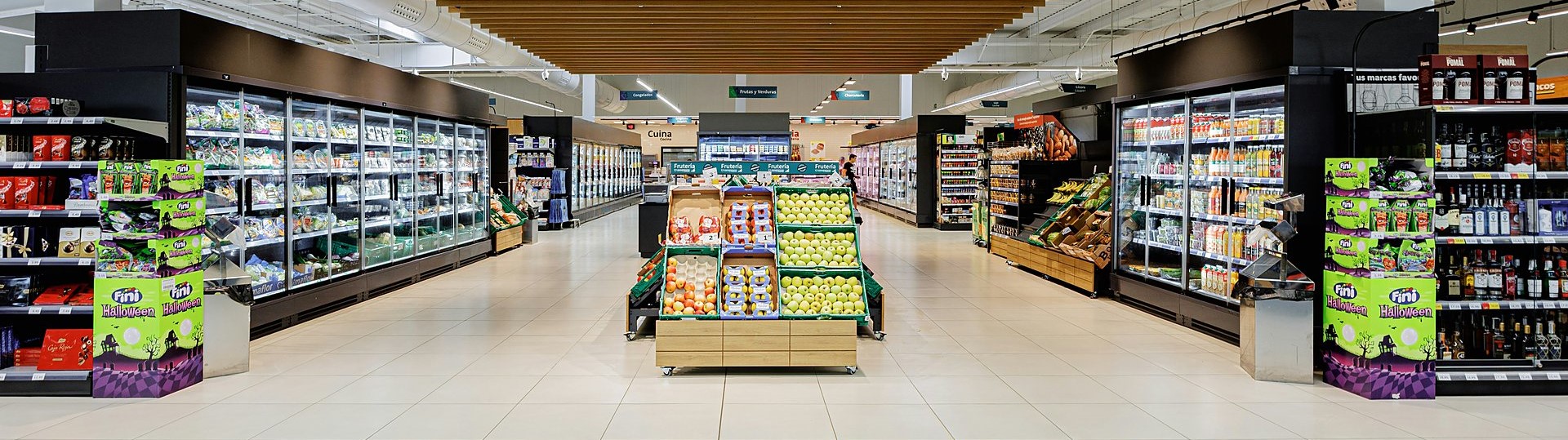 Bright supermarket interior with refrigerated aisles and a produce display of apples in the center