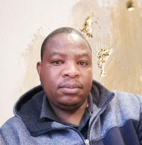 Portrait of a man wearing a gray and navy jacket with a neutral expression against a beige textured background.