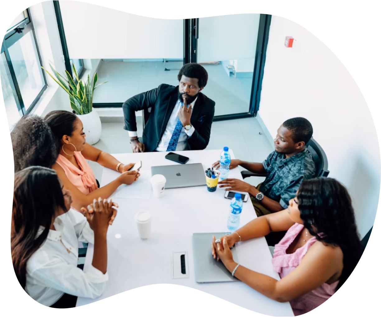 Group of four people having a business meeting around a white table with laptops, water bottles, and coffee cups in a modern office.
