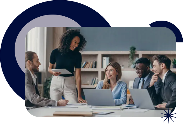 Four diverse professionals in business attire gathered around a table, collaborating and smiling in a modern office setting.