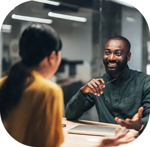 Smiling man talking with woman across table in a modern office setting.