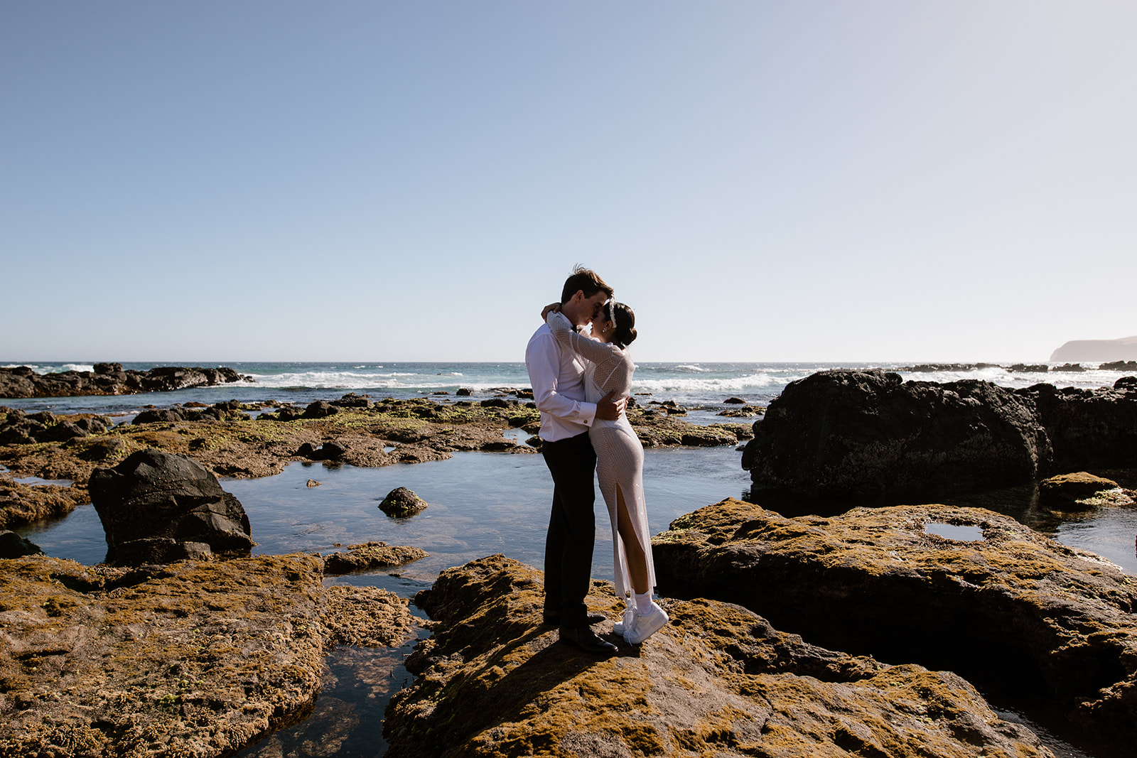 bride in bodysuit and white sneakers with groom in tuxedo