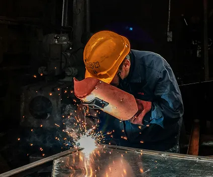 A man wearing a yellow hardhat welding something in a workshop or warehouse