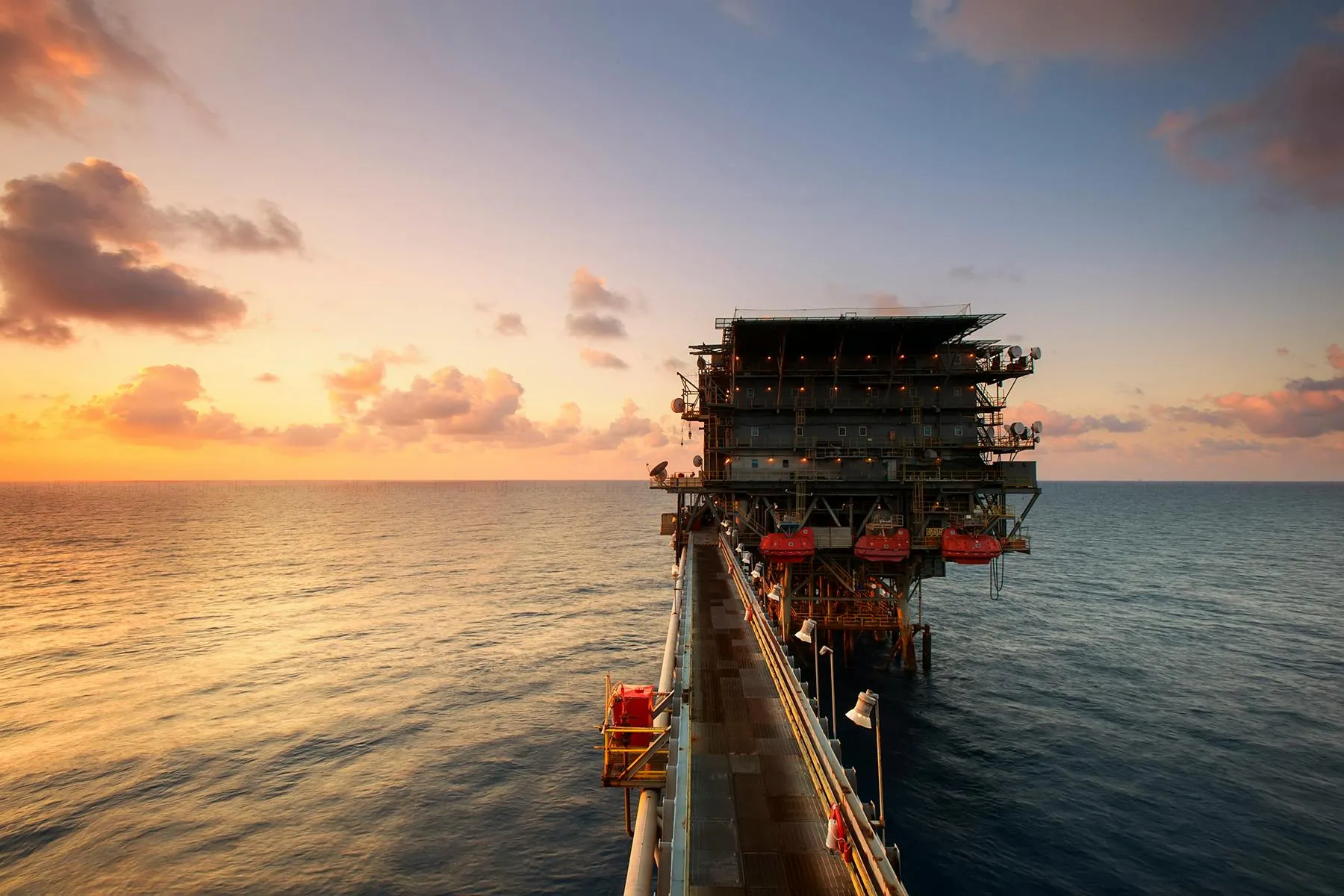 An image of an oil extraction site in the middle of an ocean during sunset or sunrise