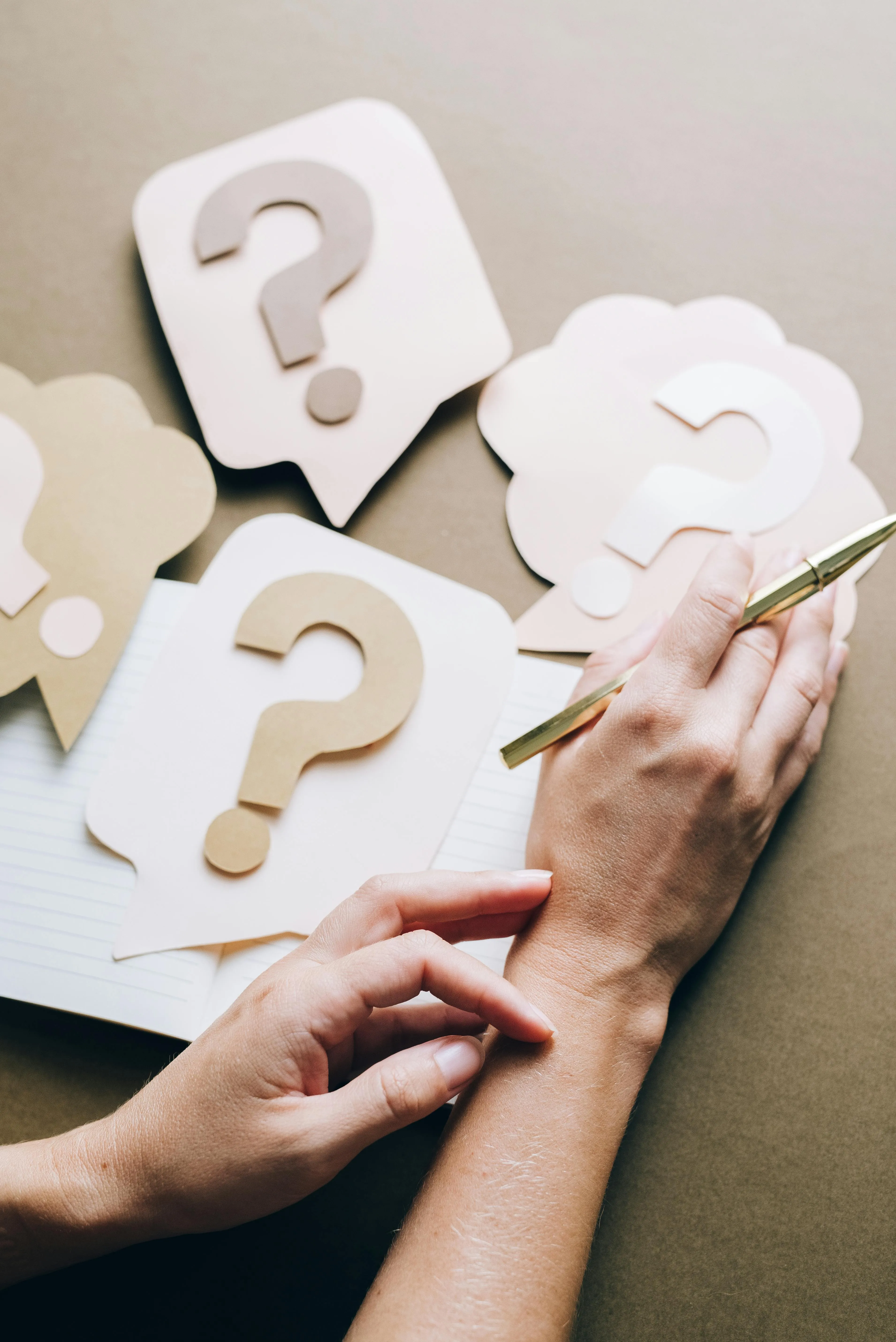 A woman sitting at a table with multiple papers having question marks on them