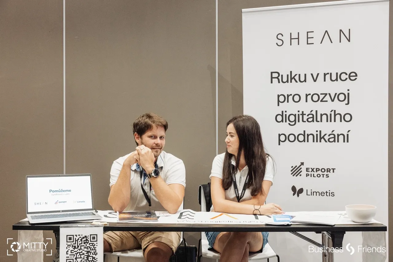 Muž a žena sedí za stolem na prezentačním stánku s bannery a počítačem k rozvoji digitálního podnikání.