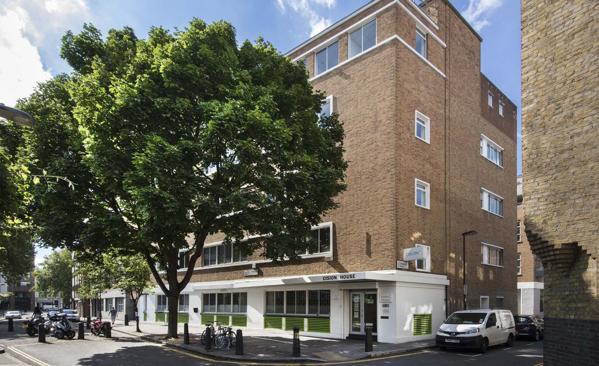 Brick office building named Cision House on a sunny street corner with trees, parked motorcycles, bicycles, and a white van.