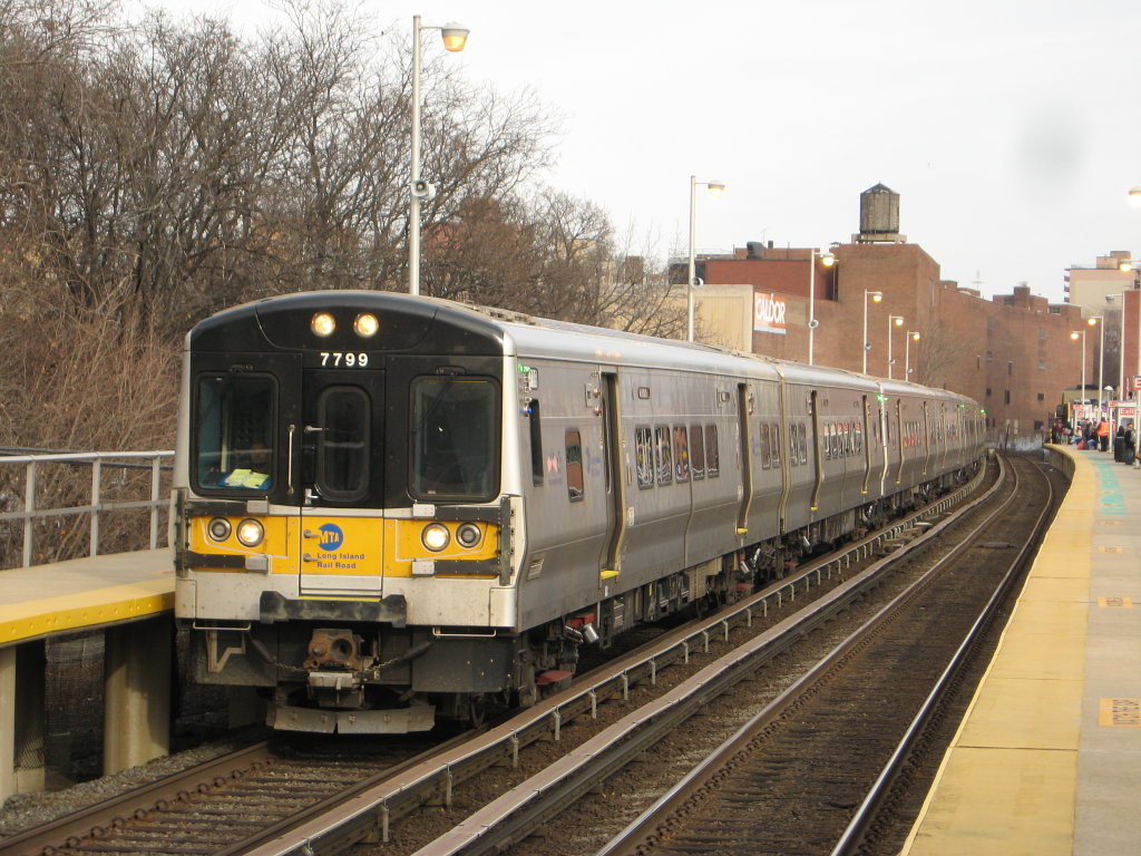 Long Island Rail Road train car number 7799 entering a station with a curved track and a platform on the right.