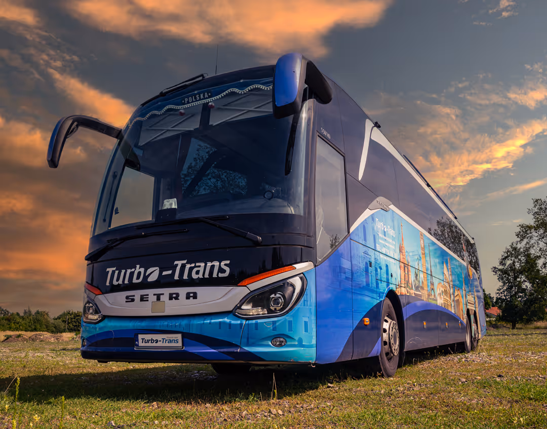 Nowoczesny autokar turystyczny Turbo-Trans gotowy na wycieczki po Dolnym Śląsku i Europie, na tle zachodzącego słońca.