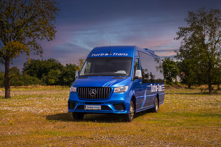 Elegancki bus Mercedes-Benz firmy Turbo-Trans gotowy do wynajmu we Wrocławiu, na tle malowniczego zachodu słońca.
