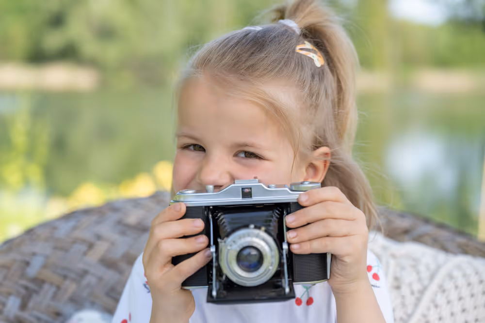 Mädchen hält eine alte Fotokamera vors Gesicht und schaut darüber hinweg