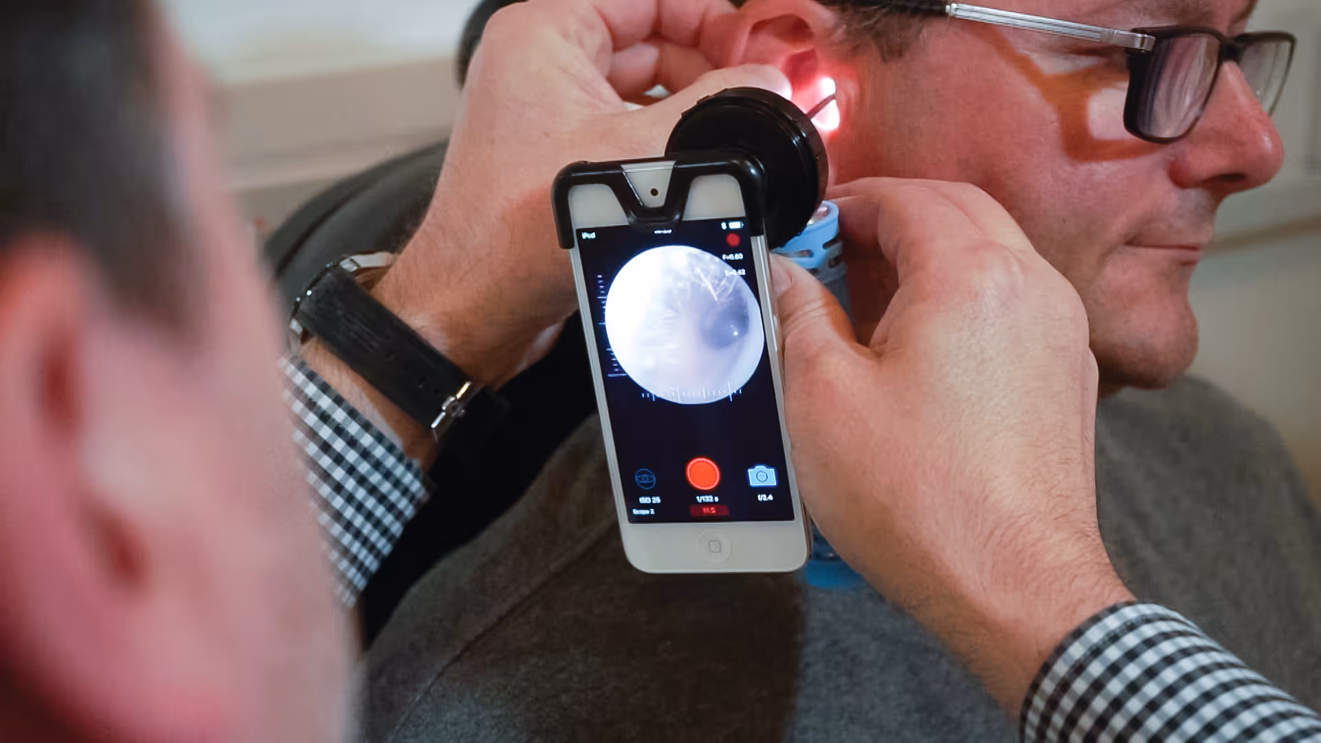 Medical professional using smartphone with attachment for ear examination