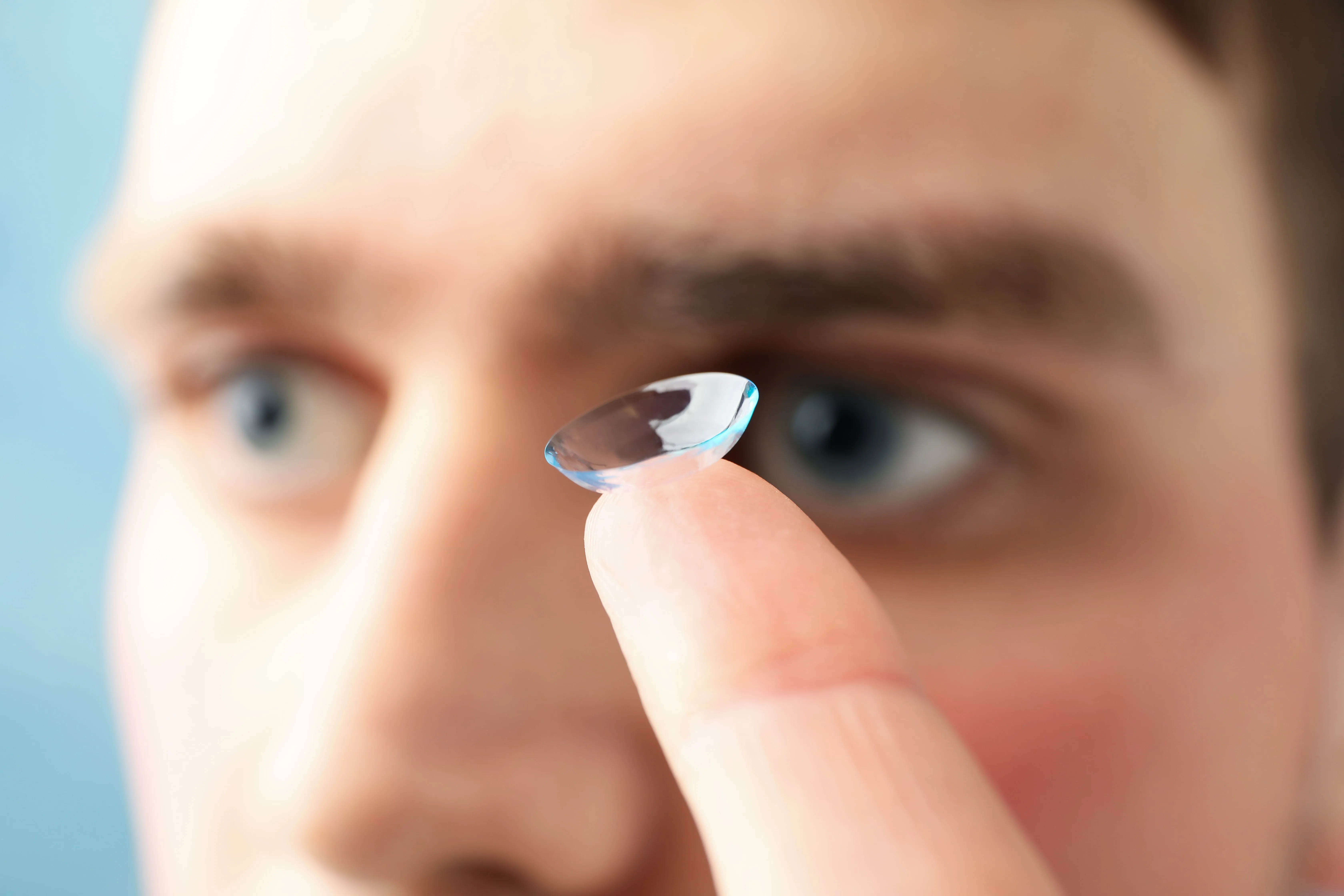 Close-up of a contact lens held between fingers near an eye