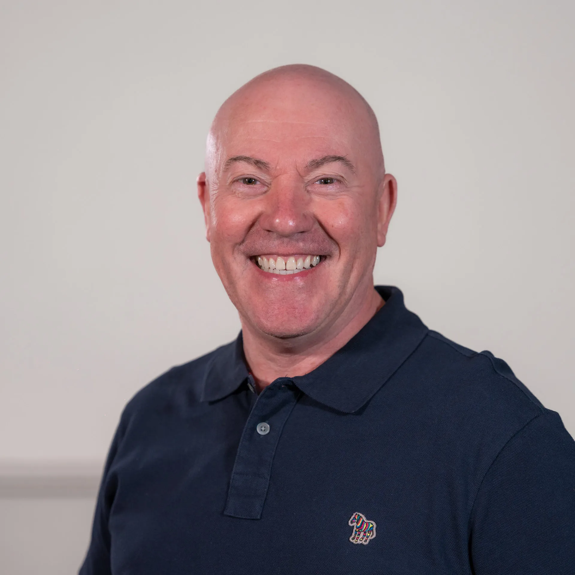 Bald man in navy polo shirt smiling broadly at camera