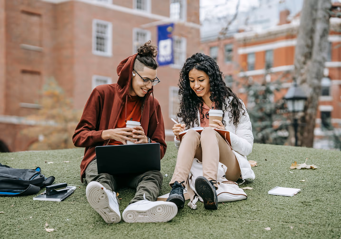 Two students writing happily while sitting on the grass