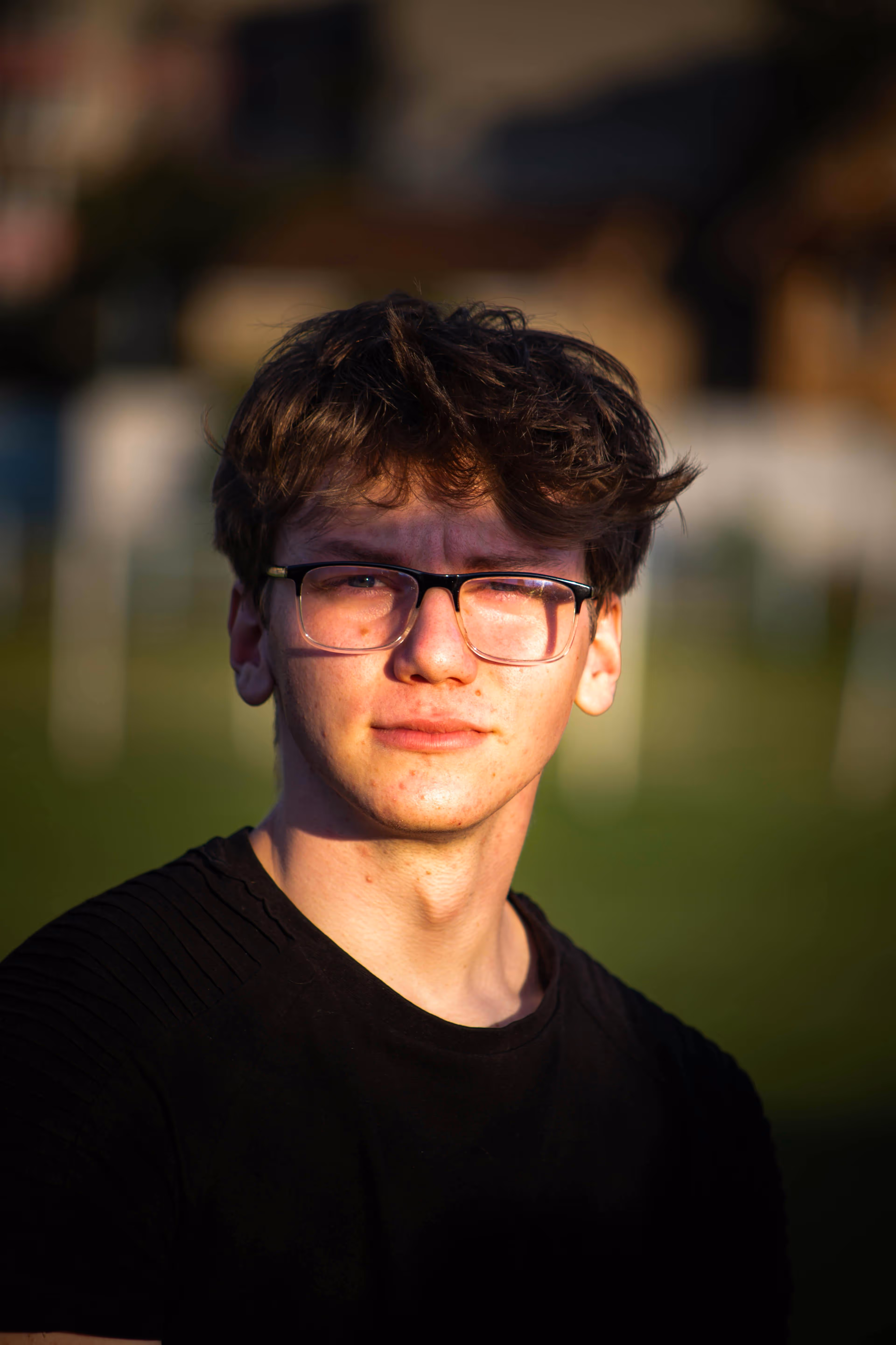 Young man with glasses wearing black shirt, blurred background