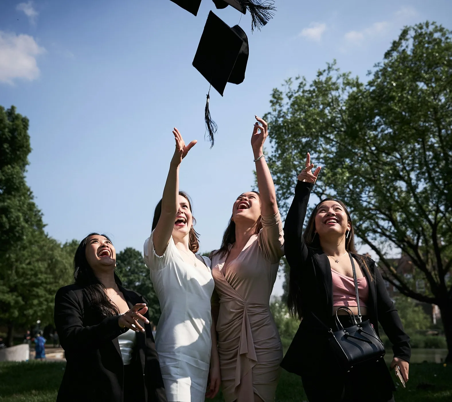 Four young women outdoors celebrating graduation by tossing their caps in the air.