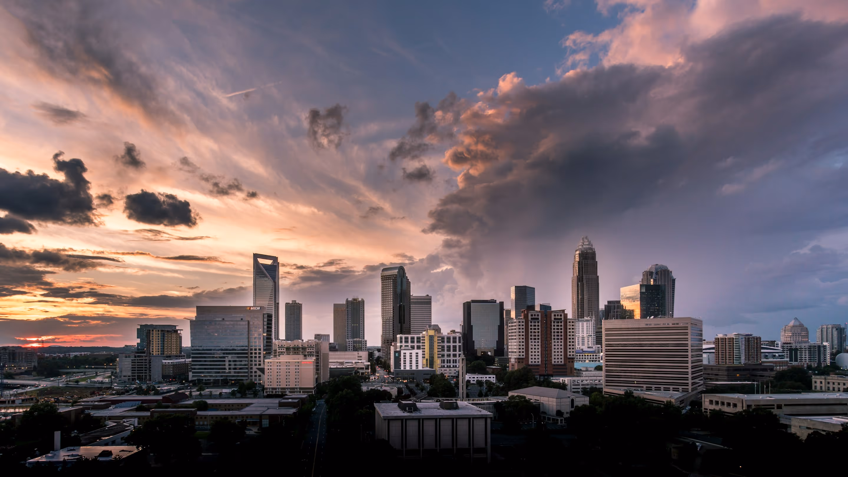 City skyline at sunset with dramatic clouds and illuminated buildings.