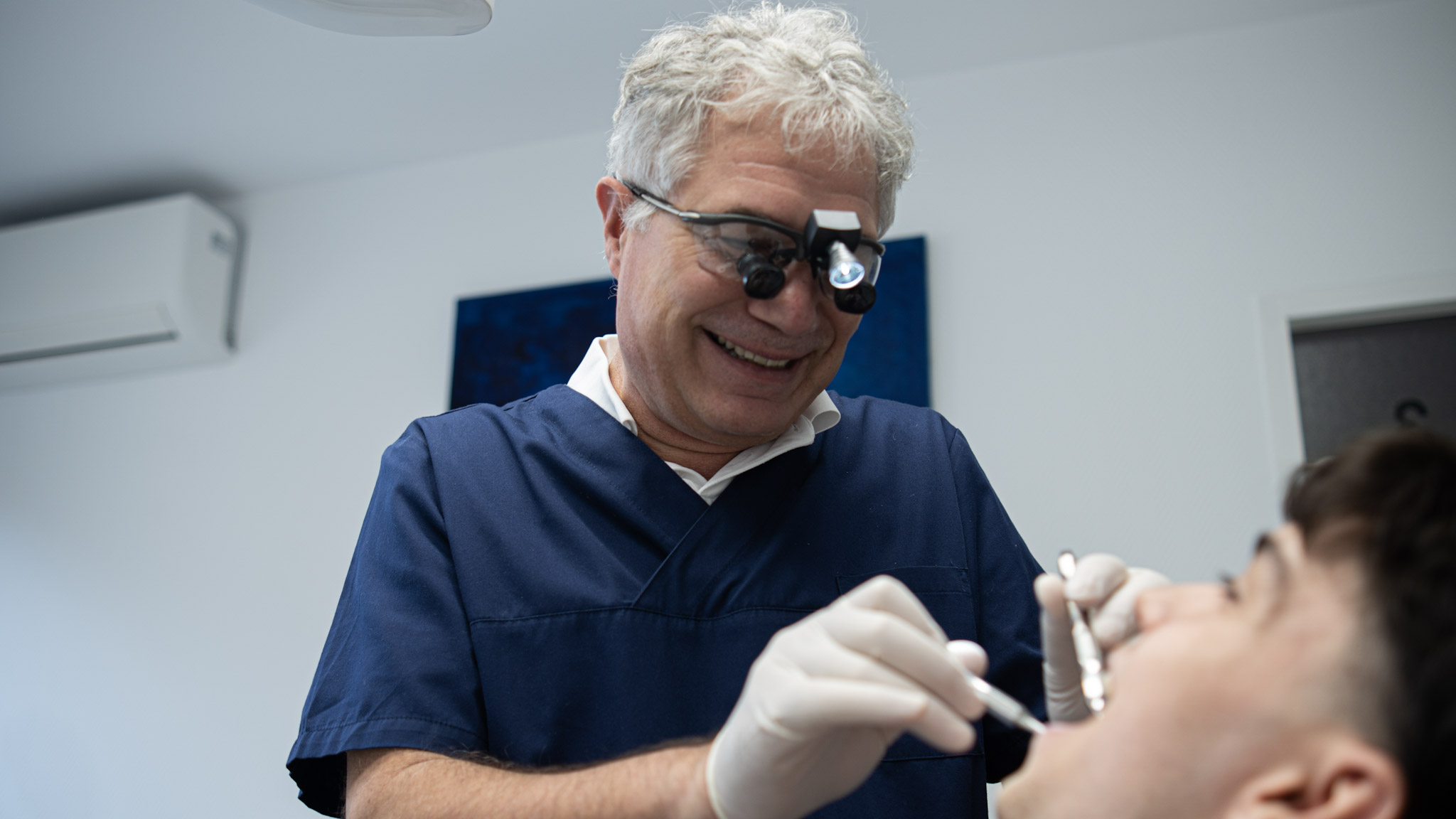 Zahnmediziner mit Lupenbrille behandelt lächelnden Patienten in moderner Praxis.