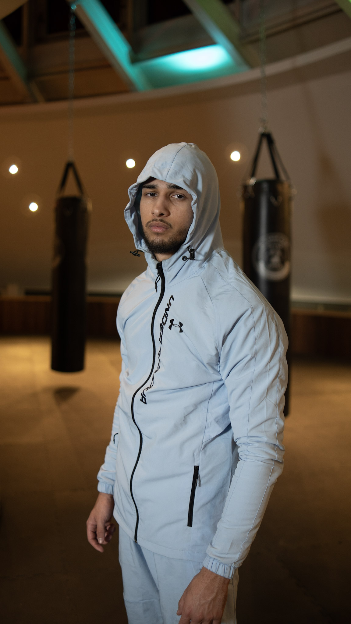 Boxer Hicham in hellblauer Trainingsjacke mit Kapuze im Gym in Bonn – konzentrierter Blick, sportliche Porträtfotografie von L’Étoile Visuals